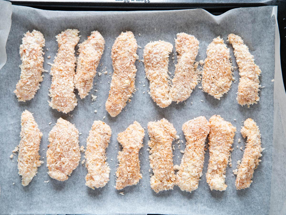 Homemade chicken goujons laid out on a baking tray, ready to cook.