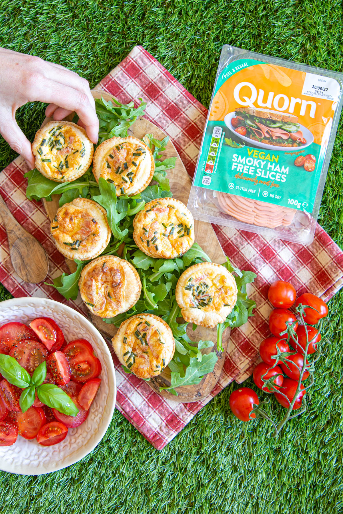 Picnic time! Mini Quorn quiche Lorraines for all, served on a wooden board alongside some juicy tomatoes. Somebody is already taking a quiche - they won't last long!.