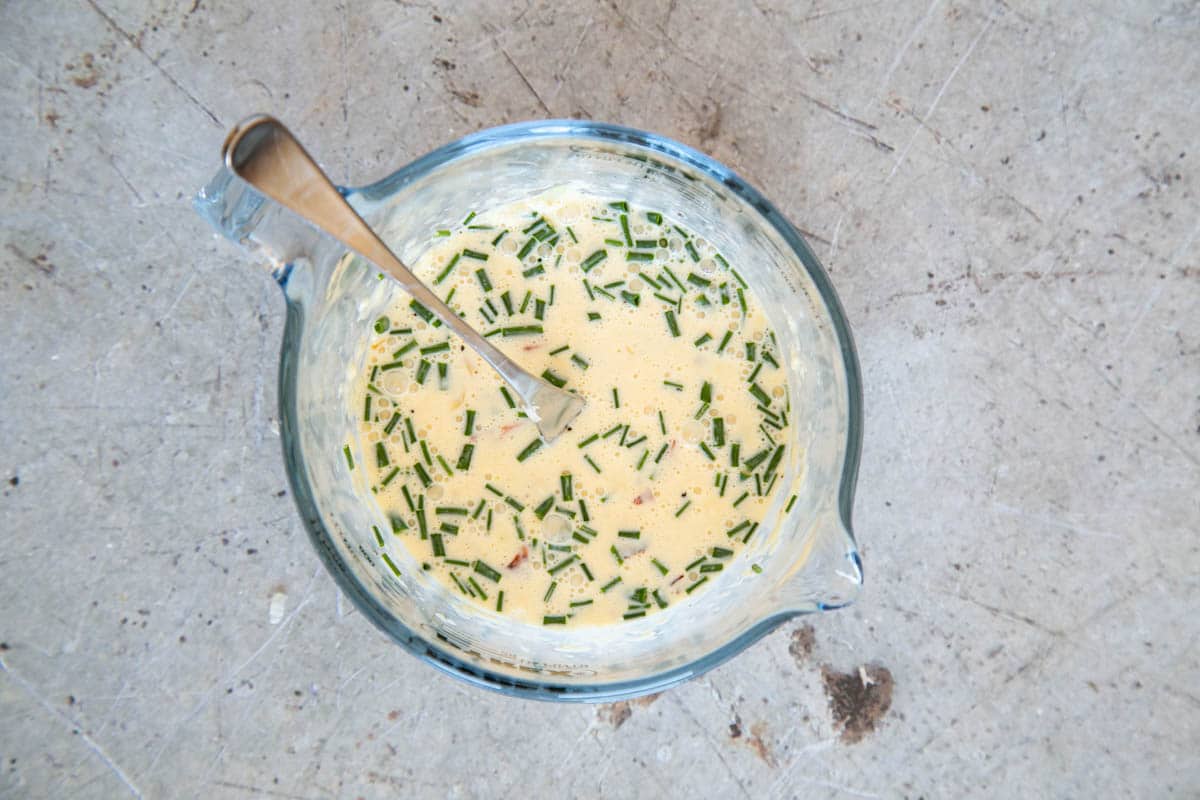 A jug of quiche mixture - cream, milk and eggs, with chopped chives floating on top.