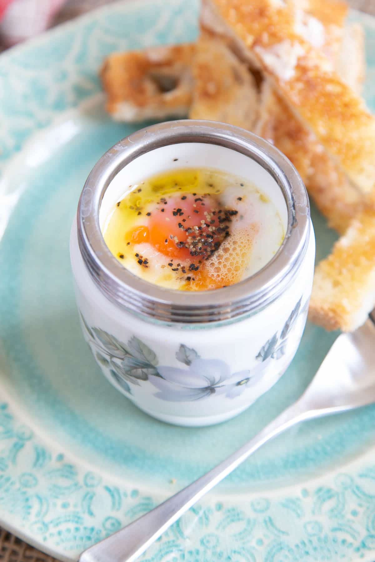 A freshly-cooked coddled egg served in an egg coddler, the yolk soft and melting, seasoned with salt and pepper.