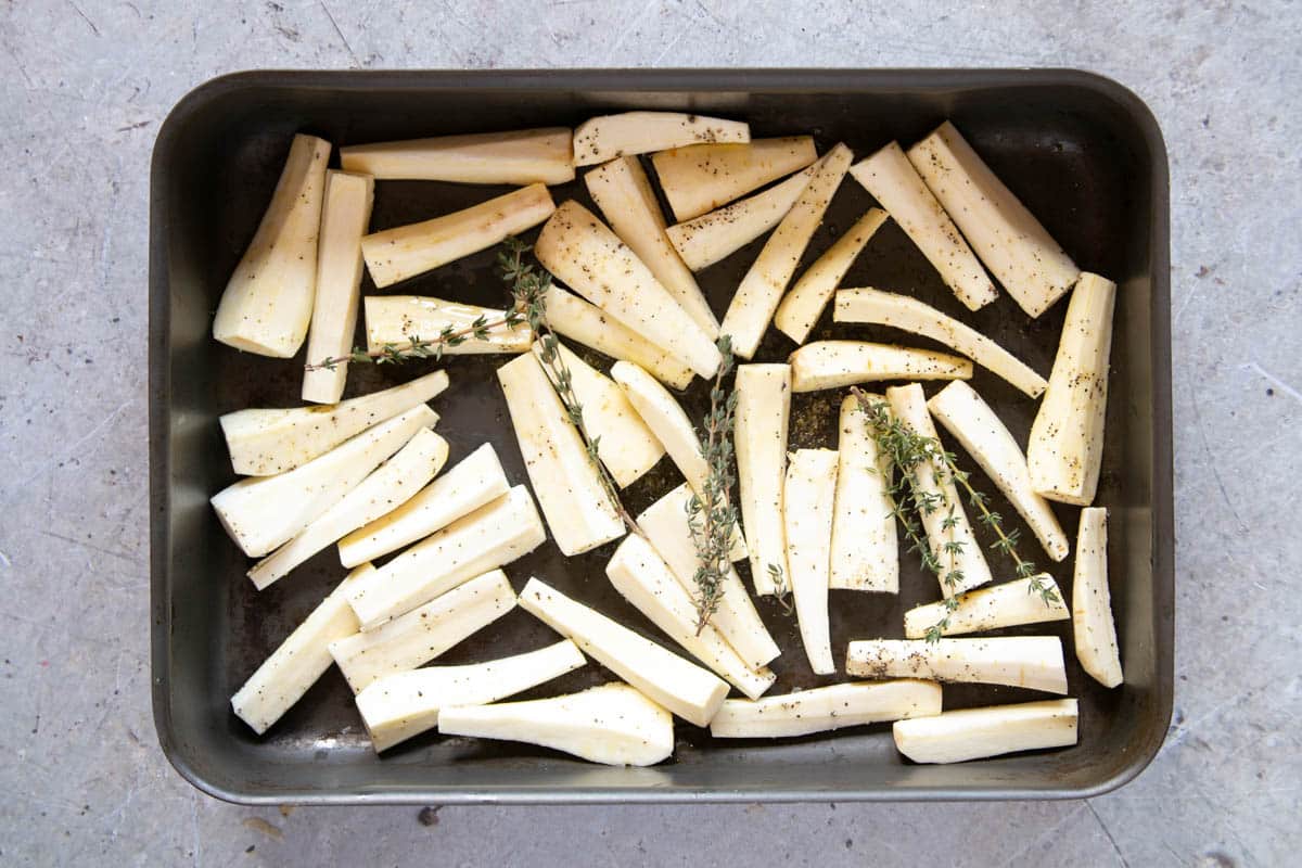 The parsnip battons spread out in a roasting tray with some sprigs of thyme.