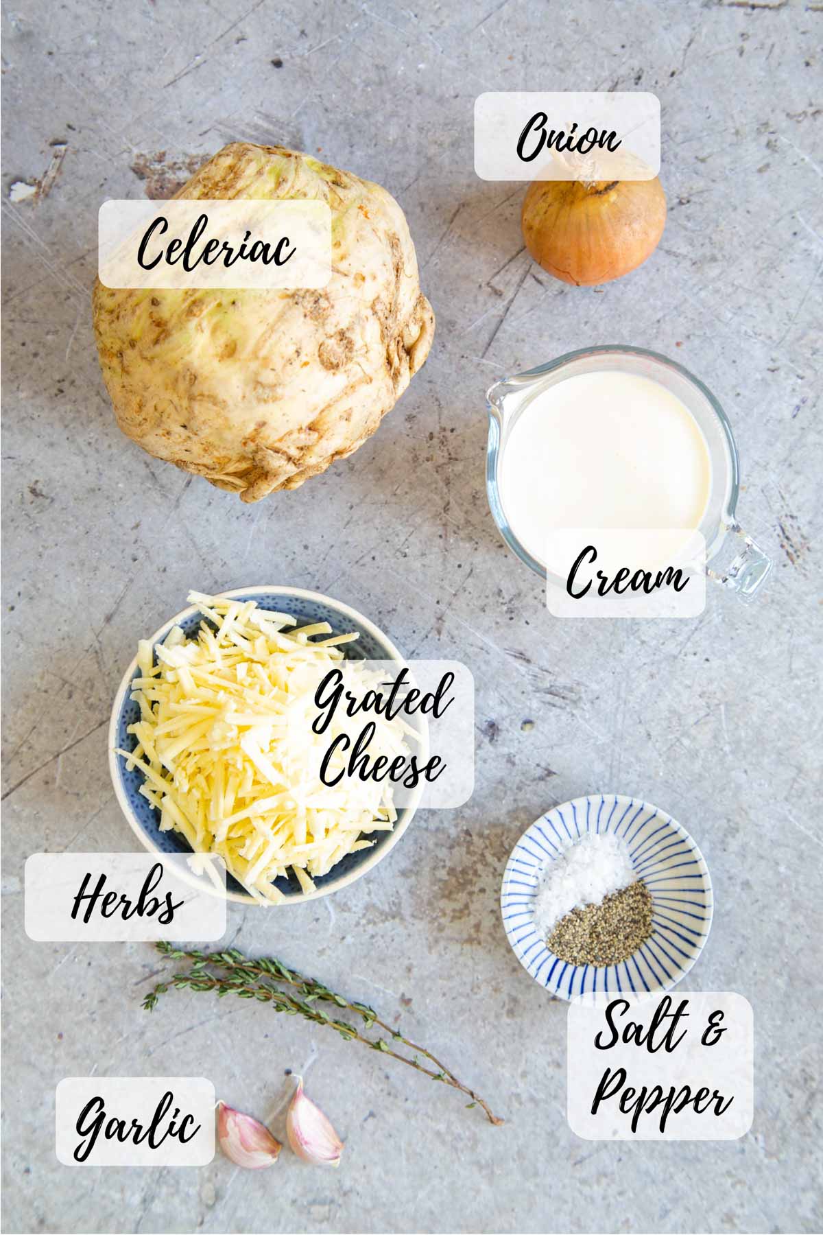 Ingredients for celeriac gratin assembled and ready to cook: celeriac, onion, cream, salt and pepper, garlic, fresh herbs and grated cheese.