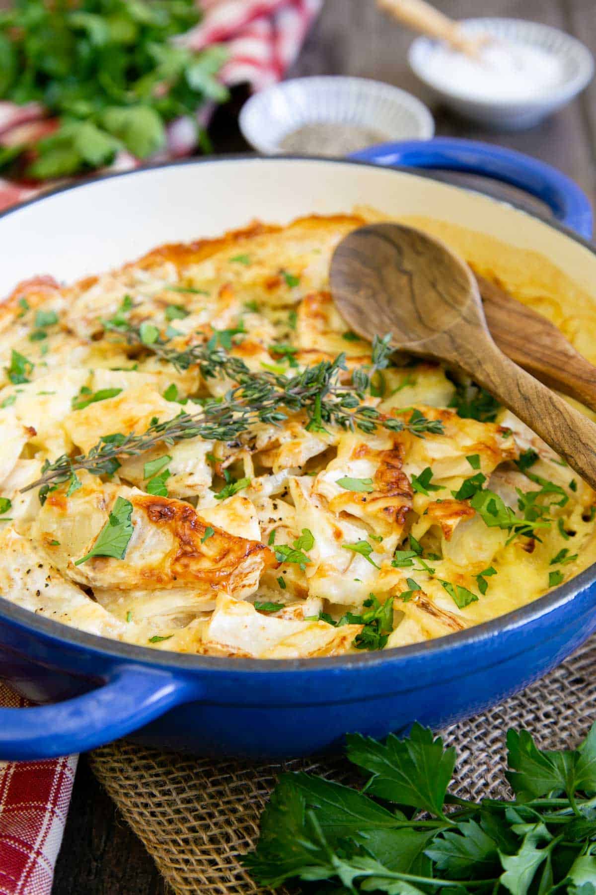 Tempting celeriac gratin in a blue stoneware serving dish, golden on the top and scattered with fresh parsley and sprigs of thyme.