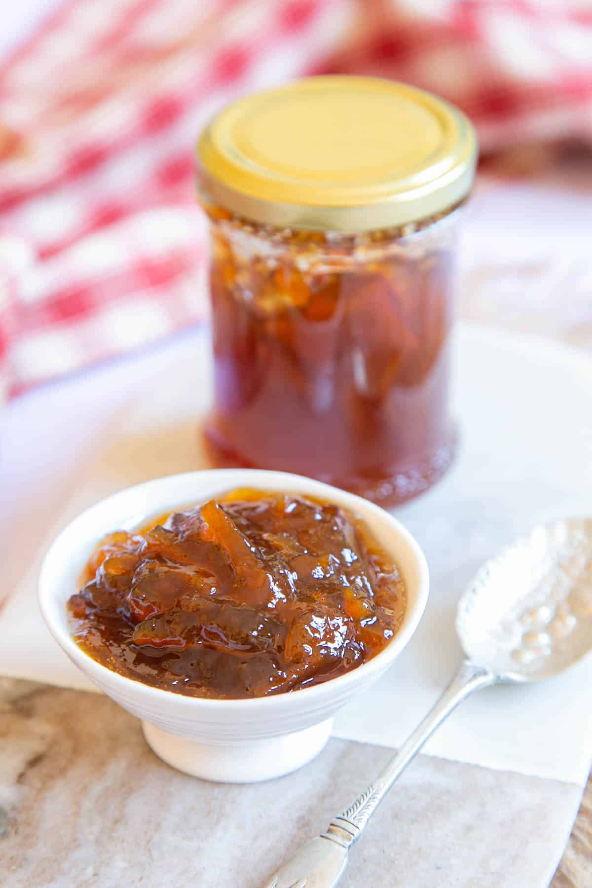 A close up of a small dish filled with marmalade. More marmalade in a jam jar is in the background.