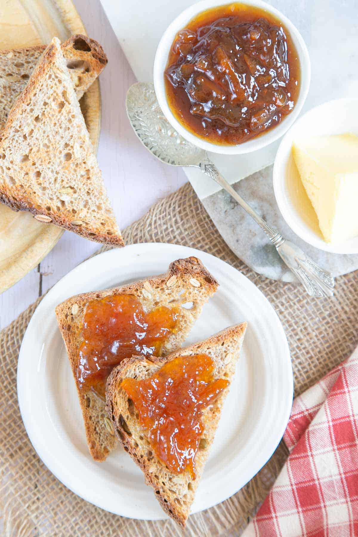 In close up, toast spread thickly with orange marmalade. More toast and marmalade are next to the two slices.