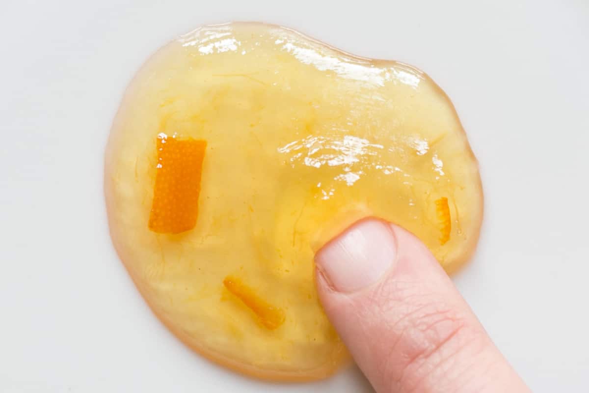 Seville orange marmalade wrinkle test. A close up of a blob of Seville orange marmalde being pushed with a finger. The marmalade is gently wrinkling ahead of the finger.
