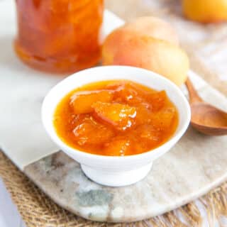 A dish of golden apricot jam, with apricots and a jar of jam in the background - breakfast is served!