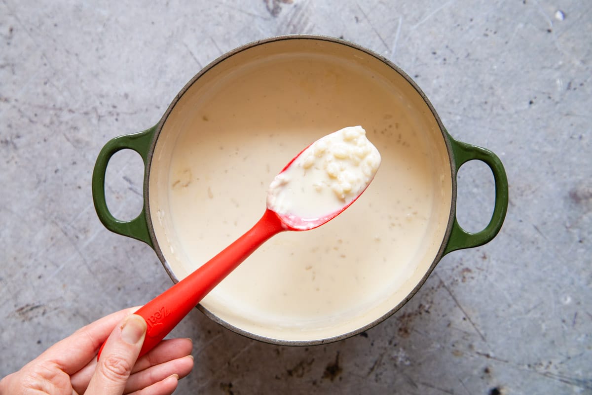 Stirring the rice pudding with a silicone spoon, carefully scraping the sides and bottom to make sure nothing sticks and burns.