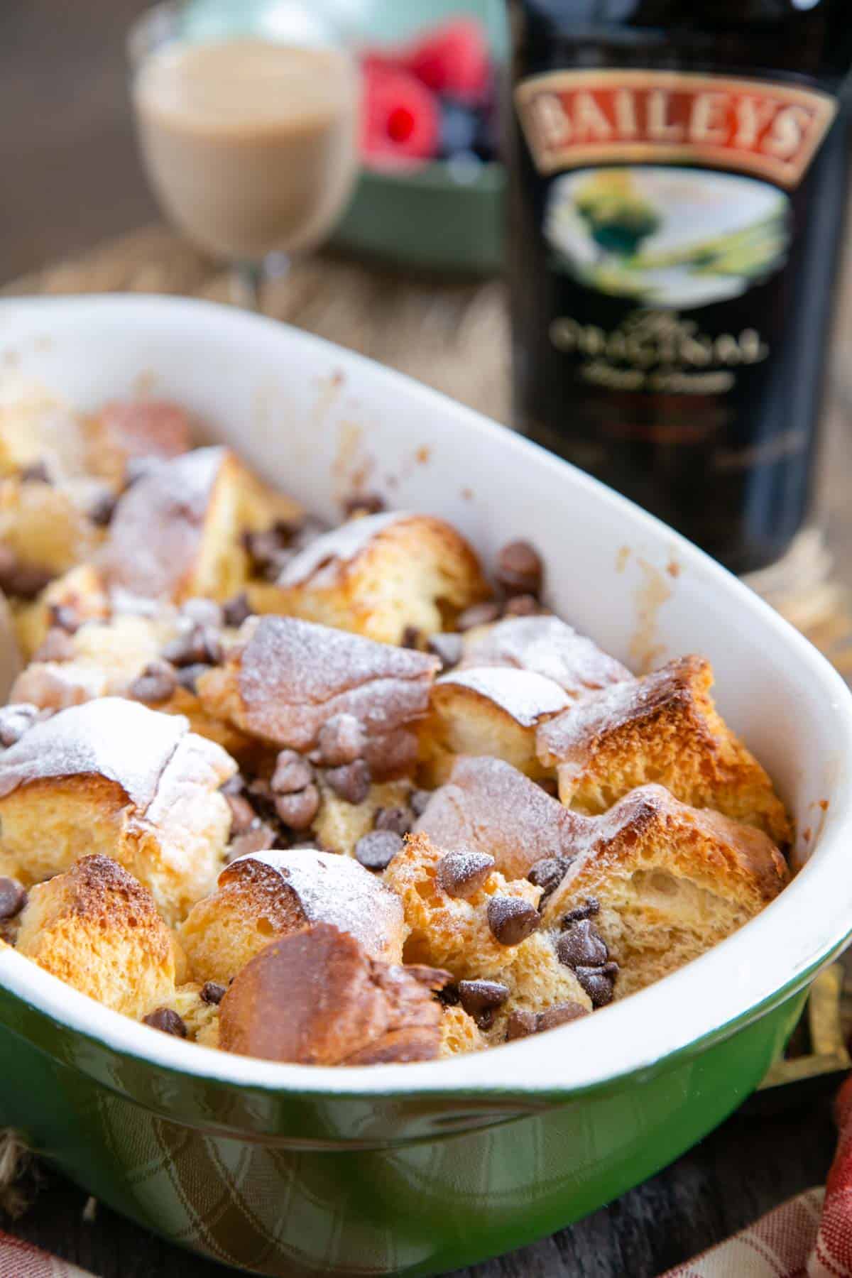 Delicious Irish cream bread and butter pudding, made with light and airy brioche. A bottle of Baileys Irish cream in the background. A close up of the dish, which has been dusted with icing sugar.