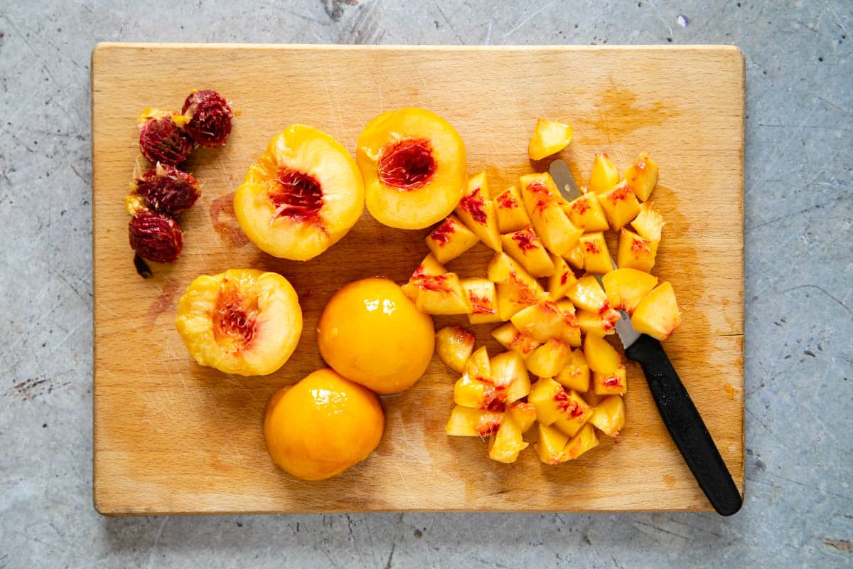 peaches being prepared for jam but cutting in half, removing the stones, and then cut into smaller pieces