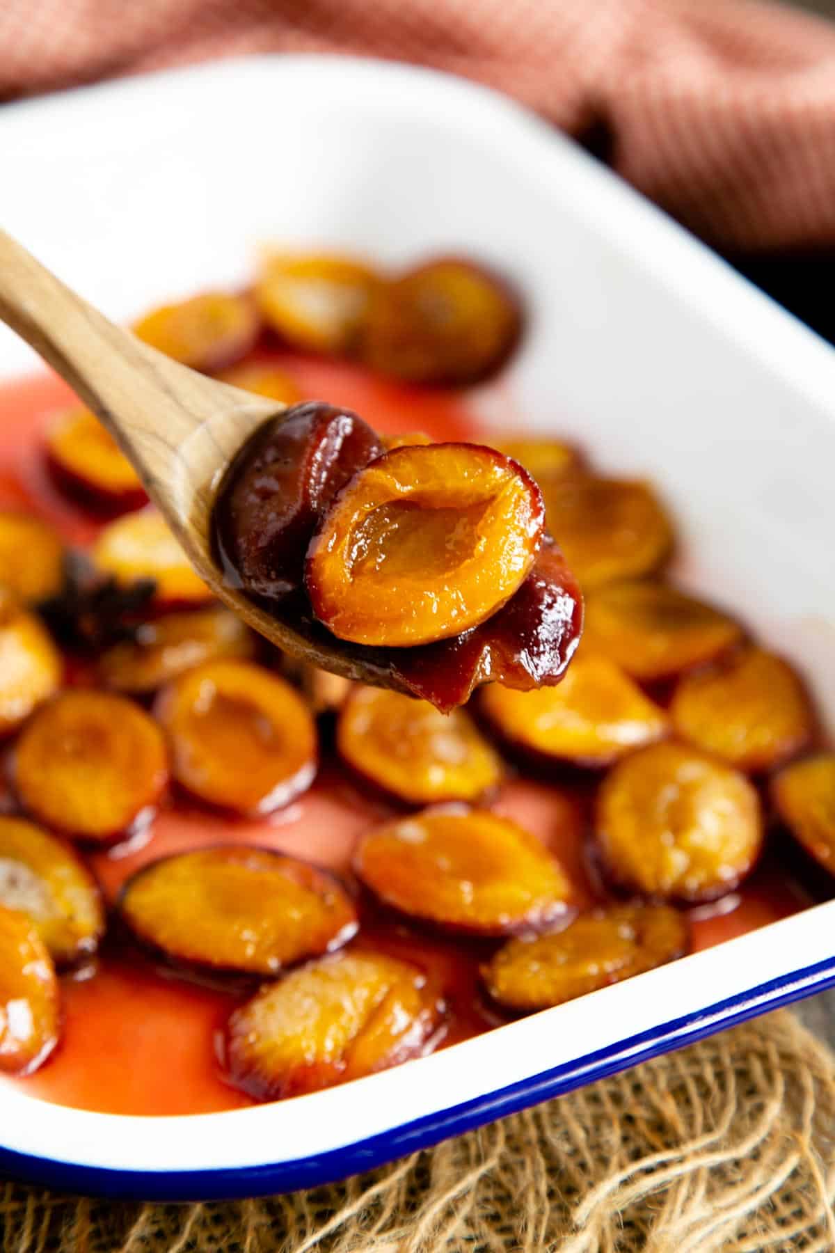 Delicious soft and flavourful roasted plums, being served from their white enamel roasting dish.