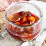 A glass jar half full of plums, in close up.