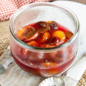 A glass jar half full of plums, in close up.