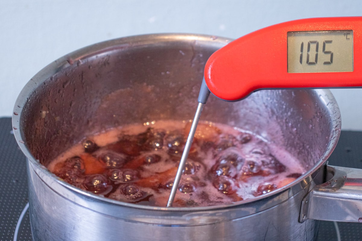 The jam is at a rolling boil, and a red digital thermometer shows that it has reached 105 degrees Celsius, the setting point.
