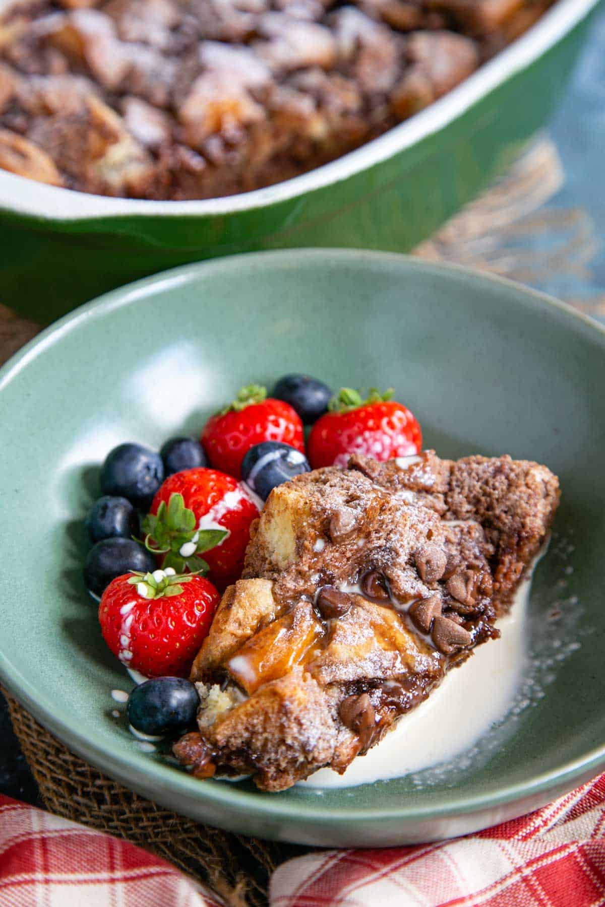 a pretty green bowl of chocolate hazelnut bread and butter pudding with fresh berries and cream
