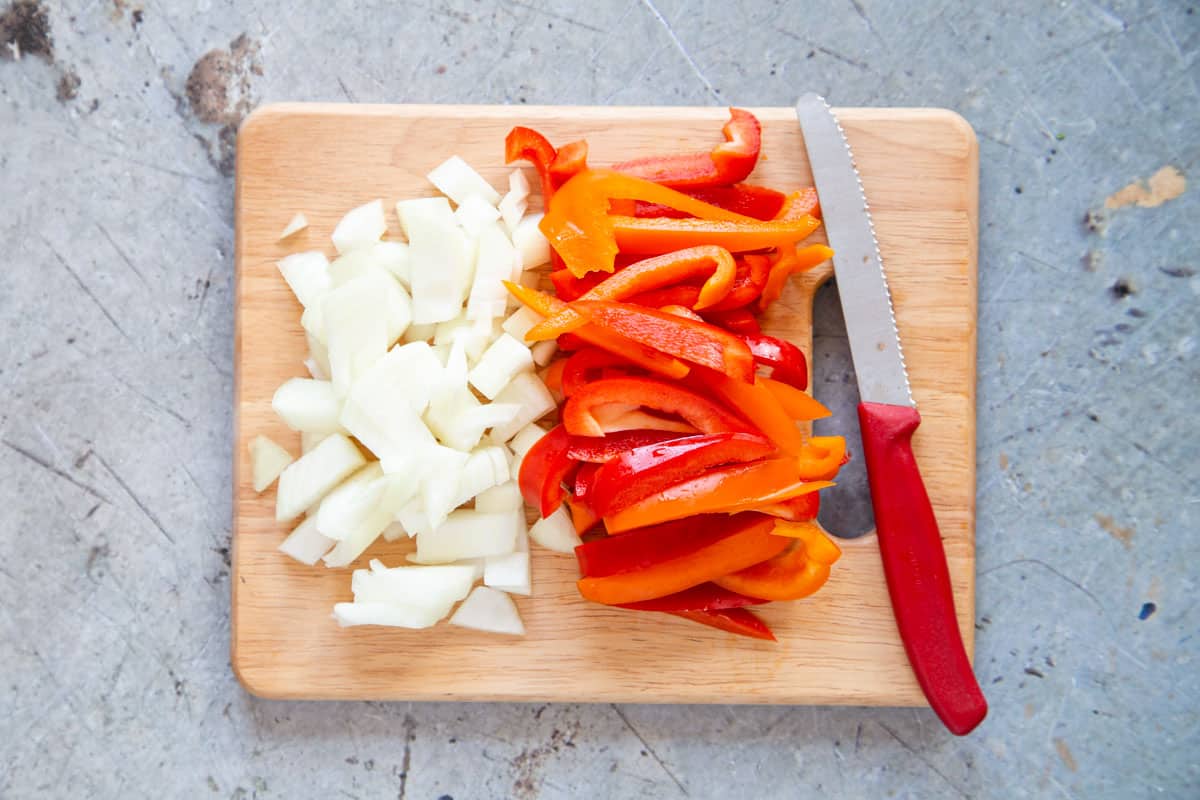 Onion and peppers cut into even sized pieces on a chopping board.