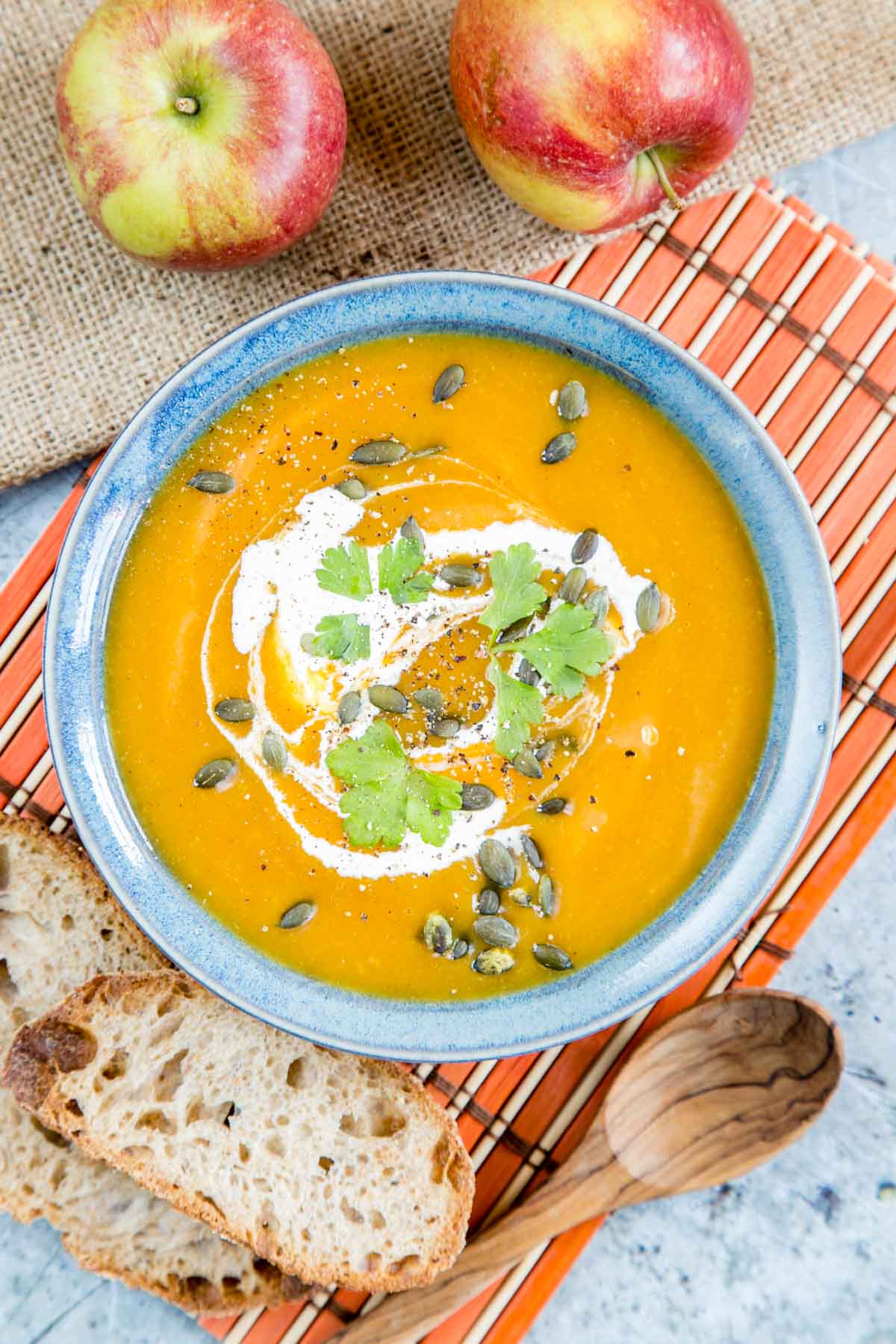 A delicious bowl of pumpkin and apple soup, golden orange and garnished with cream, parsley and pumpkin seeds, served in a contrasting blue bowl.