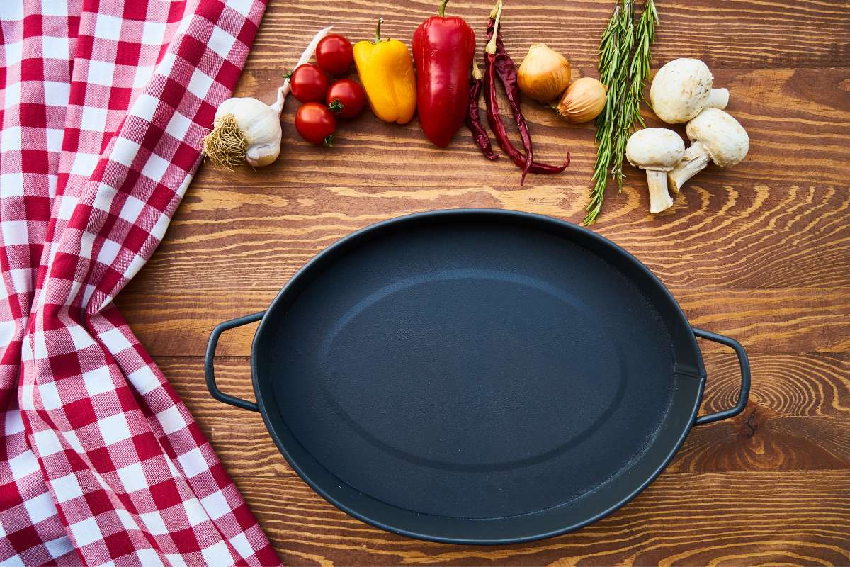 A black oval cast iron pan on a wooden surface, Ingredients are lined up above the pan, ready to cook.