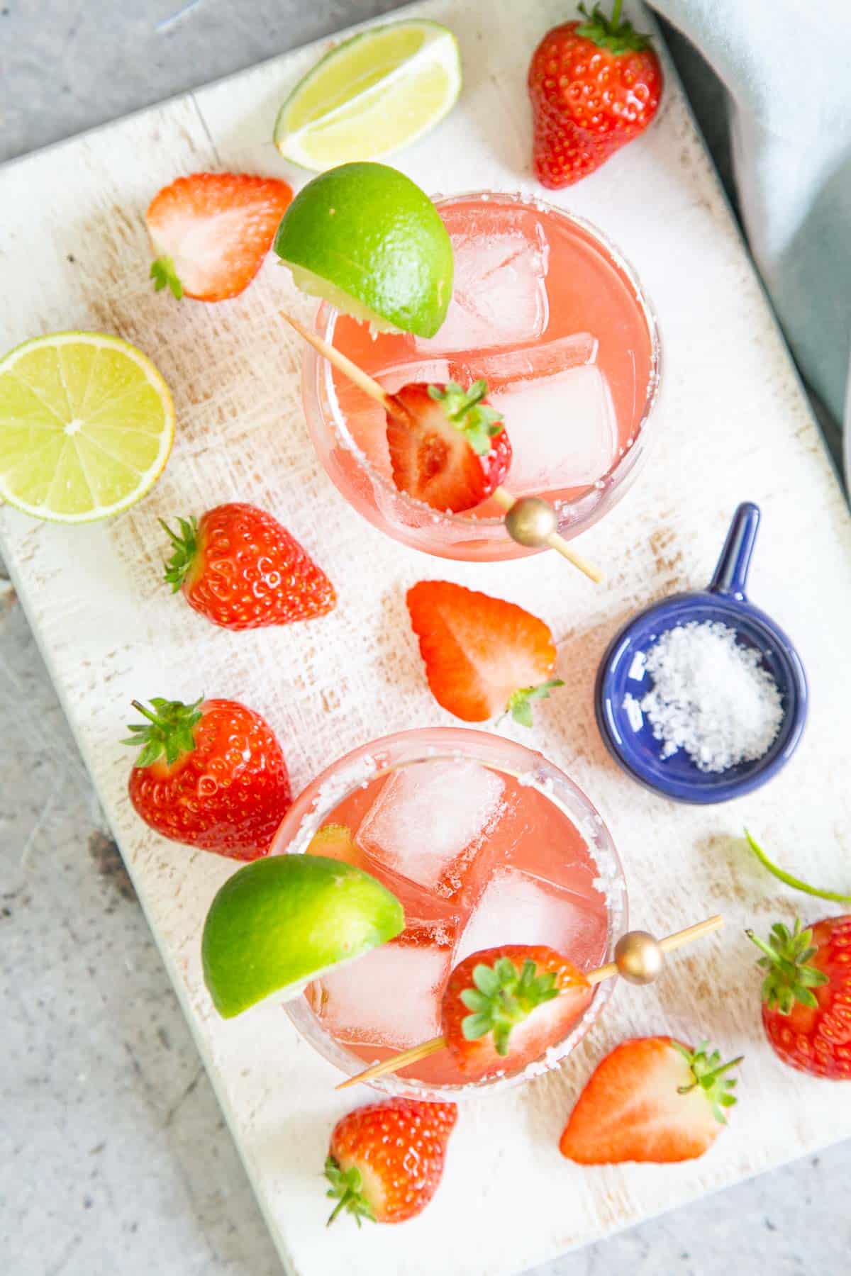 A tray with two jam margaritas, a generous fruit garnish and a pot of sea salt.