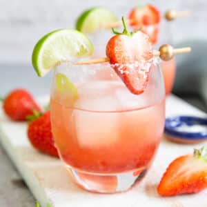 A strawberry jam margarita with ice, garnished with a strawberry and a lime wedge