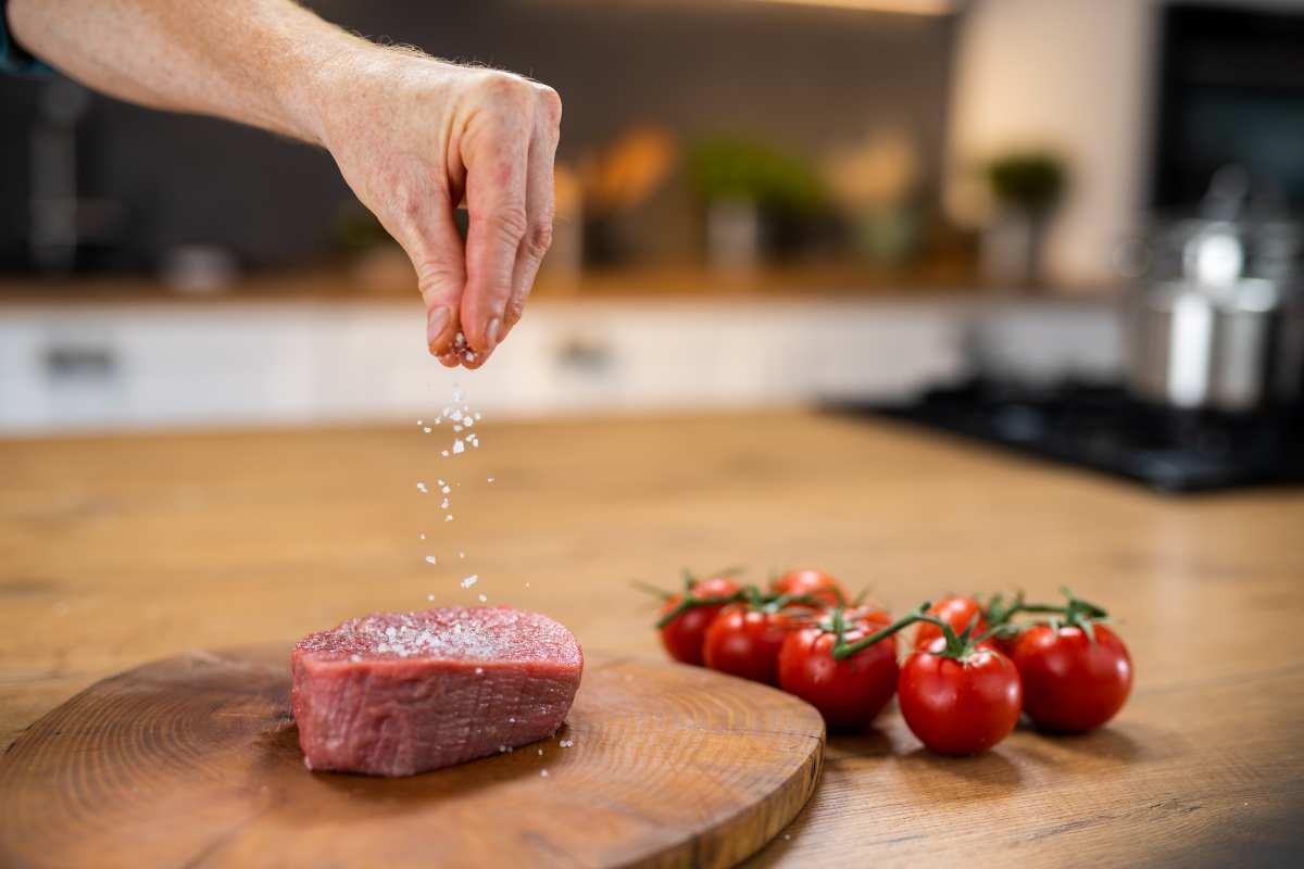 Sprinkling kosher salt on a piece of raw red meat.
