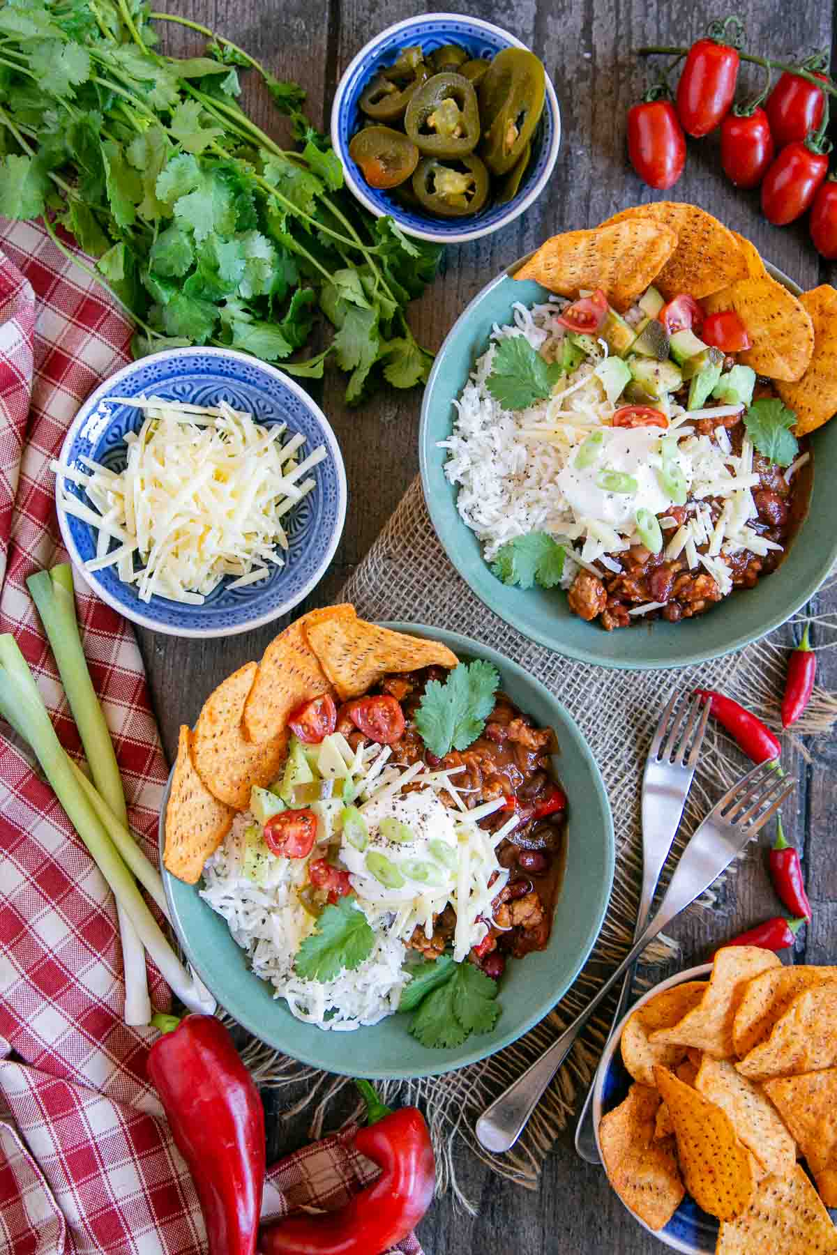 Bowls of slow cooker ground turkey chili with a range of toppings - cheese, spring onions, pickled chilies and more.