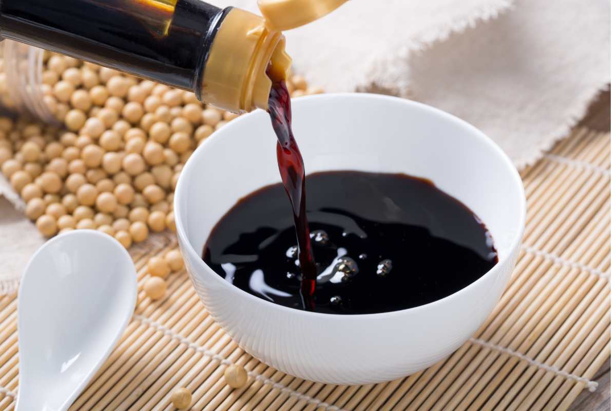 Pouring Japanese soy sauce into a small bowl, with dried soy beans in the background.