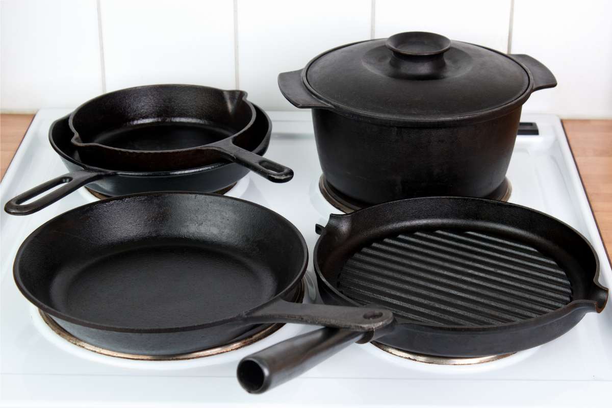 A range of cast iron pans: frying pans, skillets, and a Dutch oven, all on an electric hob.