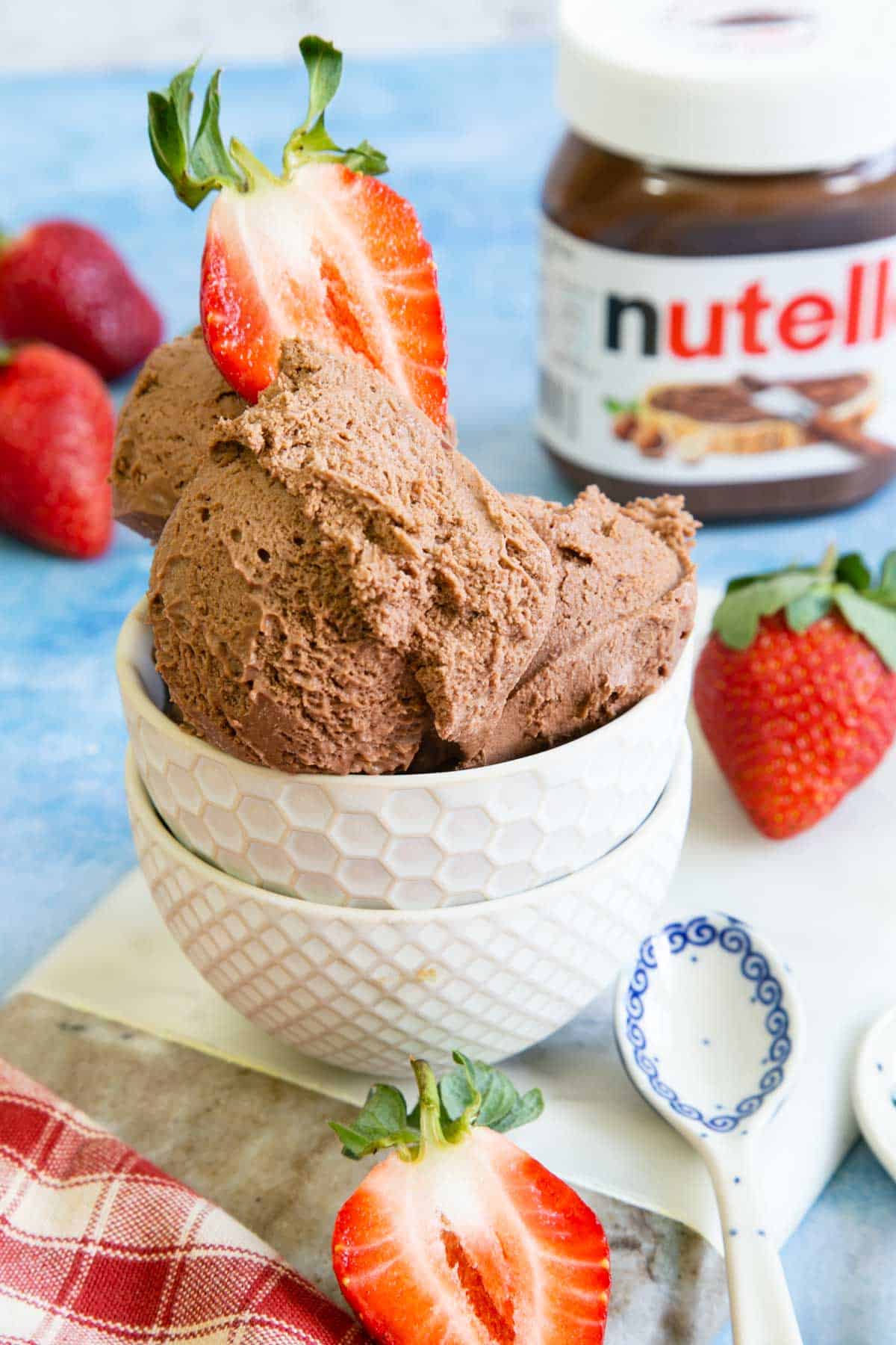Nutella ice cream served in dainty white dishes, with a jar of Nutella and some strawberries in the background.