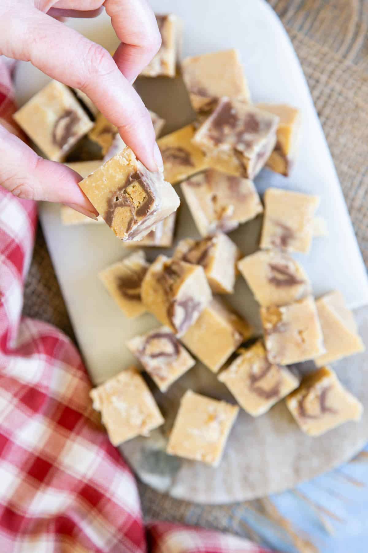 A hand lifting a piece of fudge from a platter.