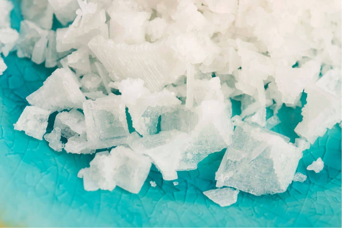 Large, easily crushed flakes of fleur de sel contrast with a turquoise blue background.