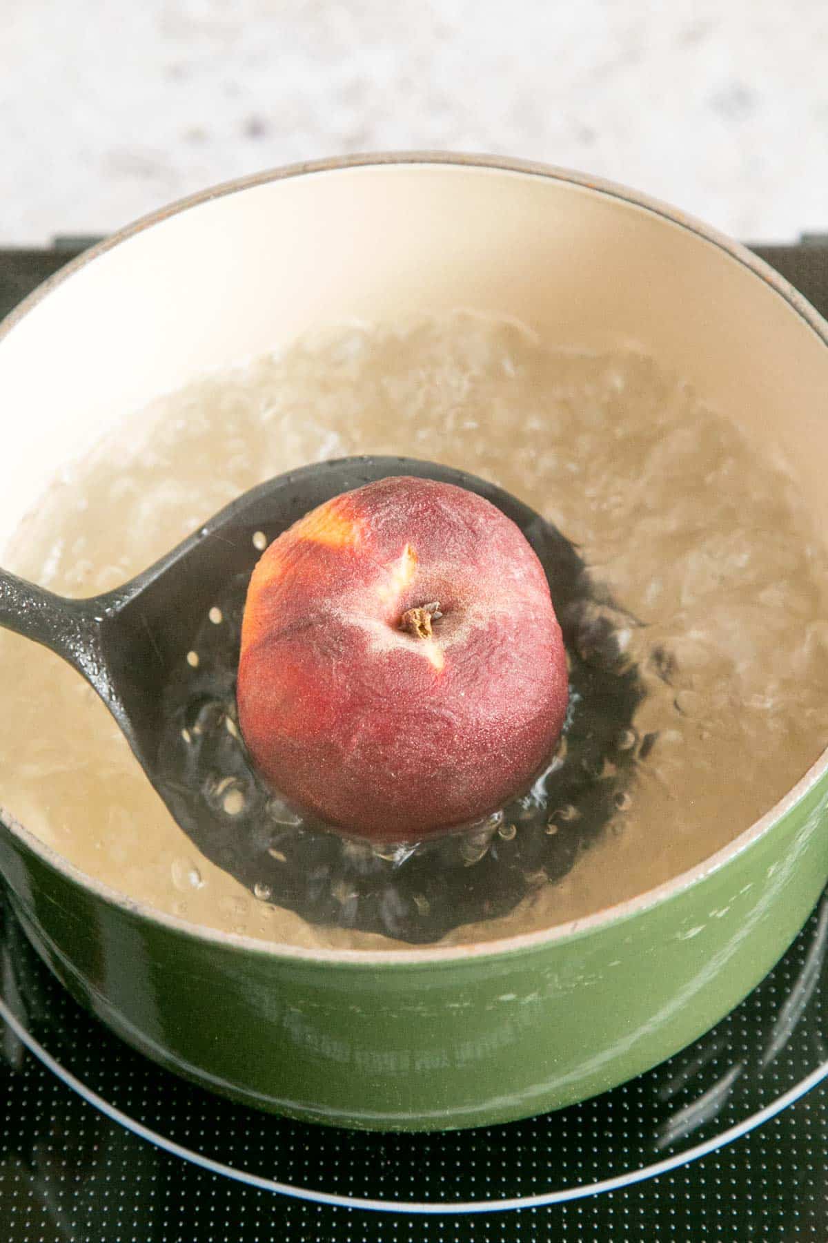 Lowering a peach into a saucepan of water.