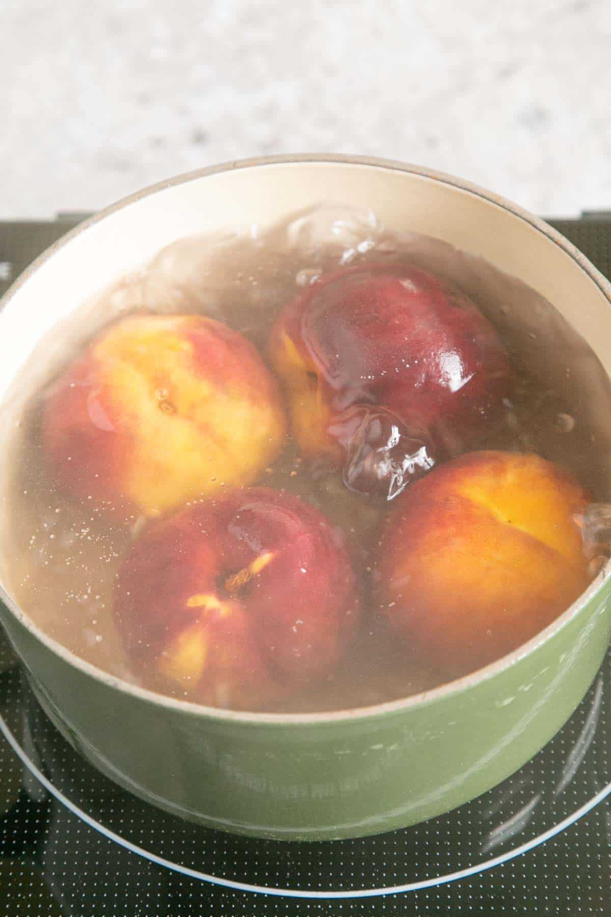 The peaches submerged in boiling water.