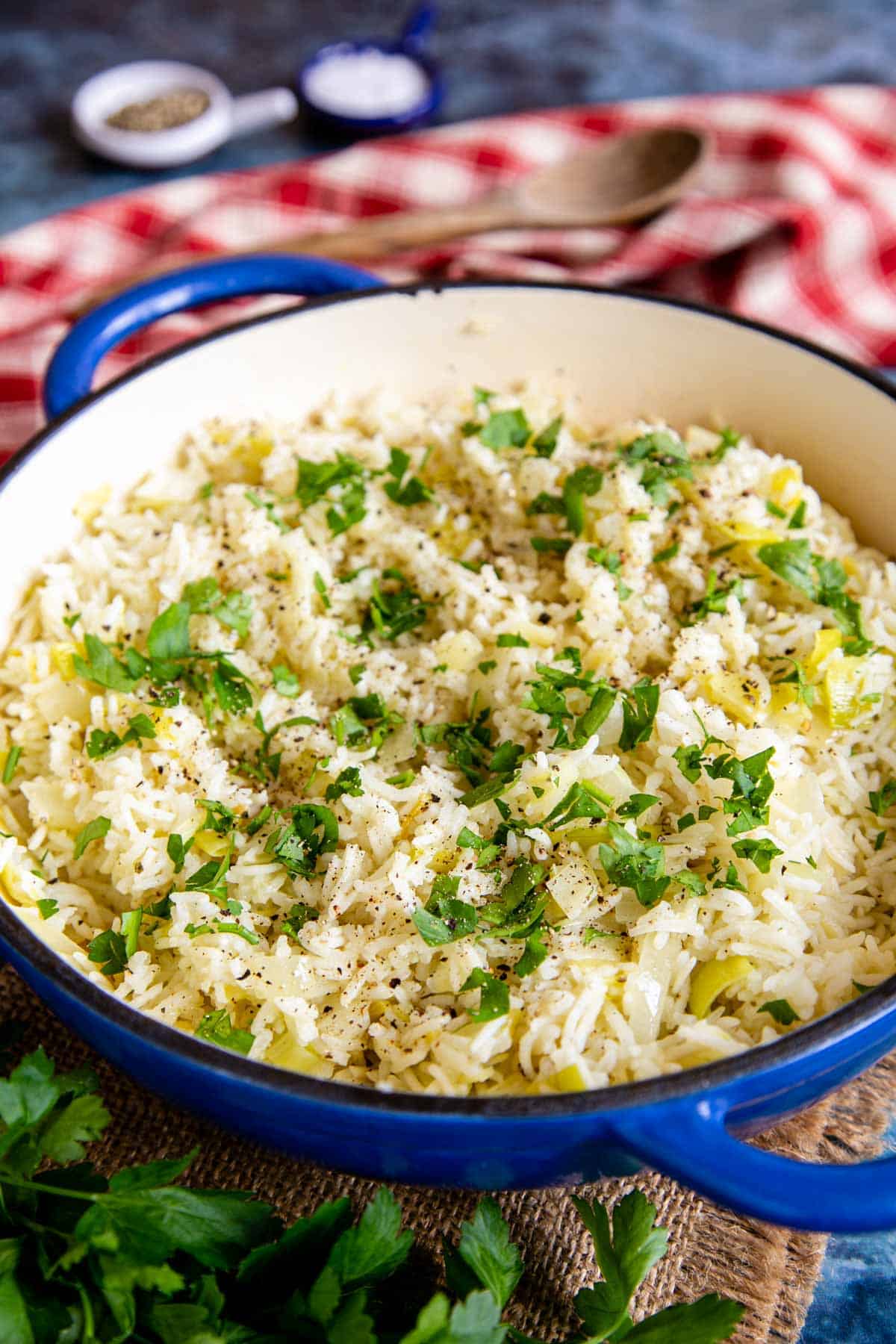 Tender leek rice served with a scattering of dark green parsley in a blue and white casserole dish against a red gingham cloth.