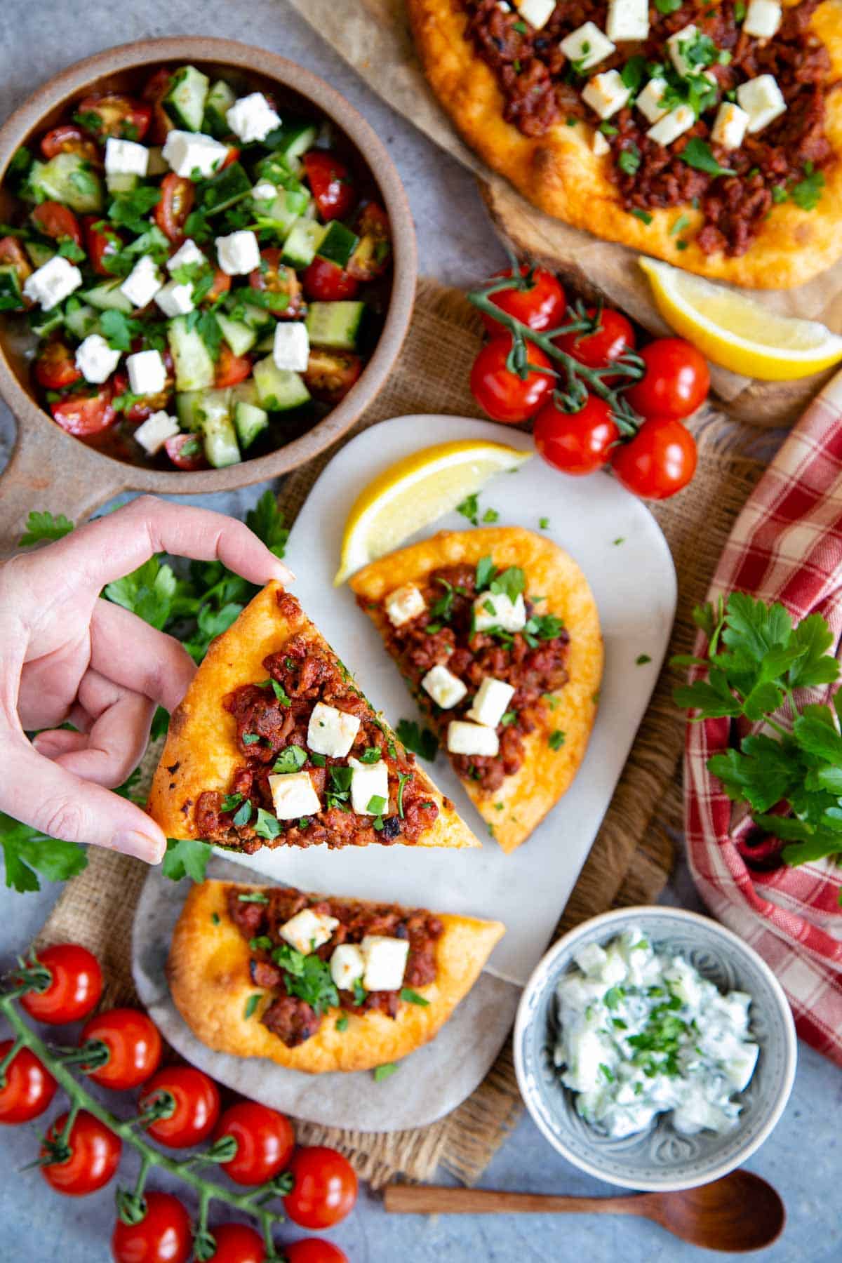 Mince pizza or lahmacun, served on a marble board with Greek salad, tzatziki and tomatoes