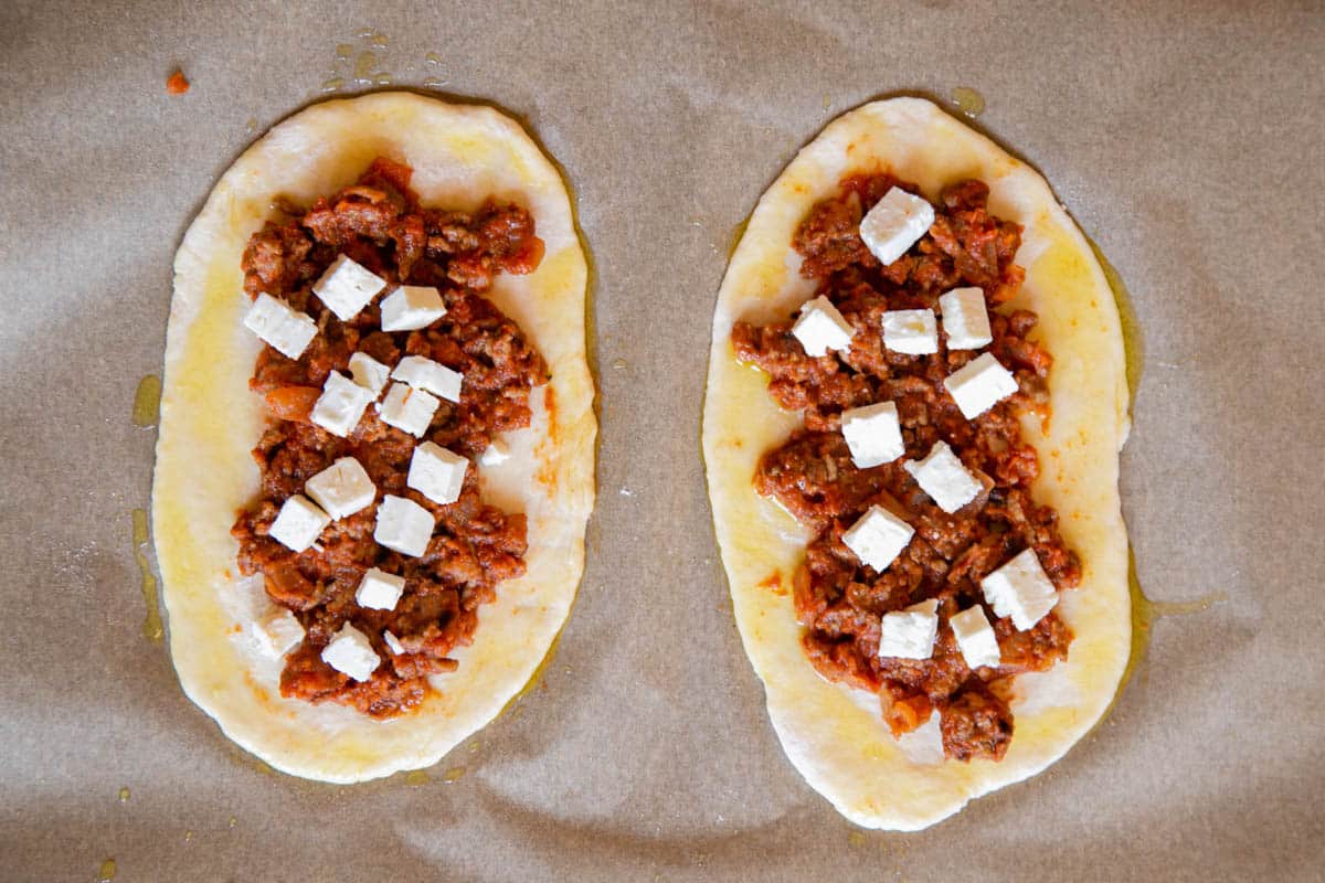 The meat sauce on the uncooked flatbread dough, with a sprinkle of feta on top, ready for the oven.