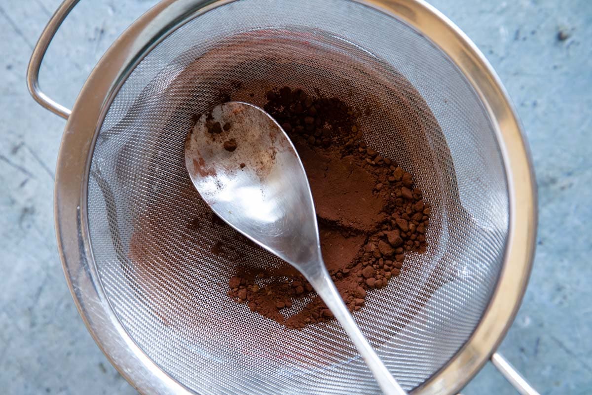 Sifting the cocoa, using the back of a spoon to force any lumps through the sieve.