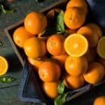 A wooden box full of oranges, with orange leaves scattered around.