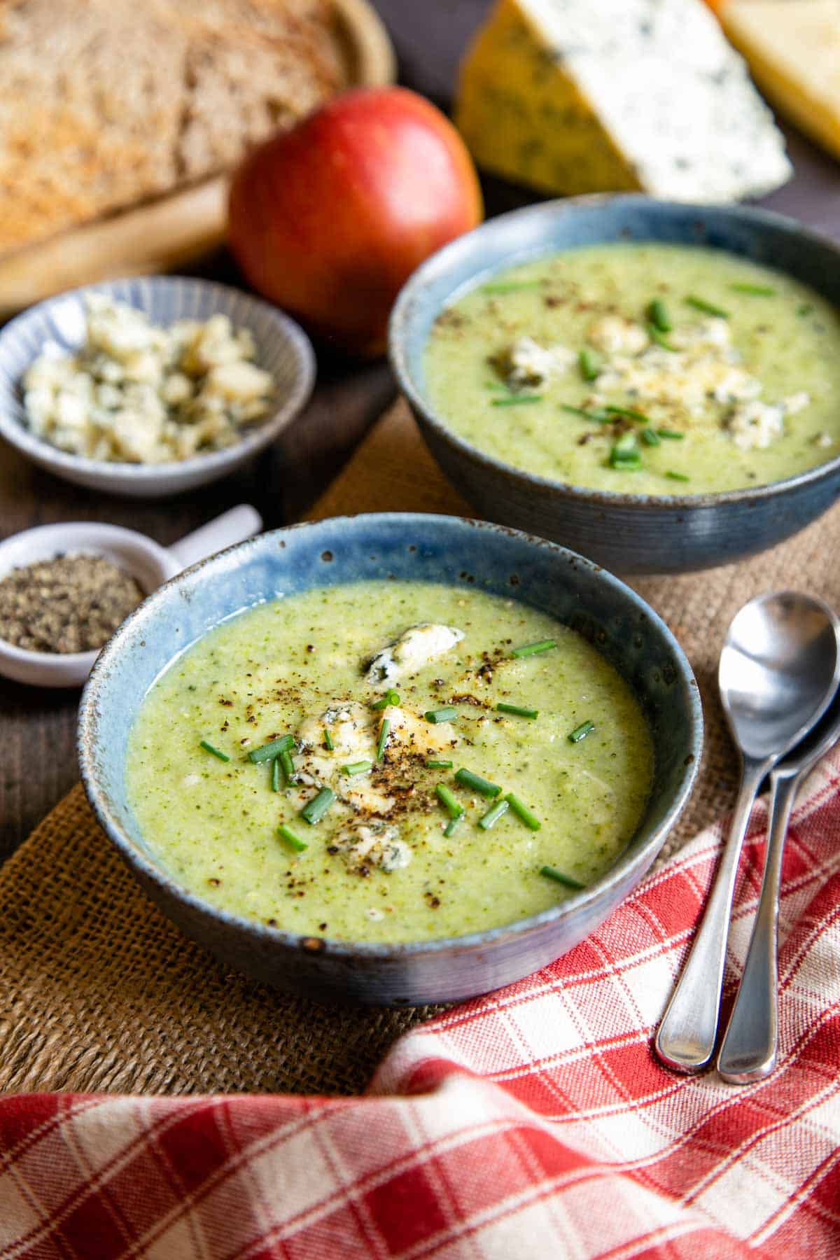 Dishes of enticing green broccoli and stilton soup, served with cheese, apples and toast.