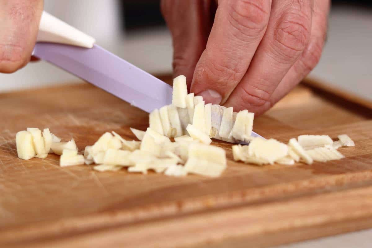 A close up of garlic being chopped on a wooden board.