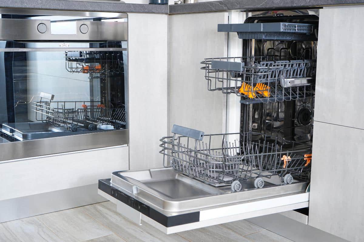 A clean, empty and open dishwasher in a modern, light and bright kitchen. The machine is open, ready to receive dirty plates and cutlery.