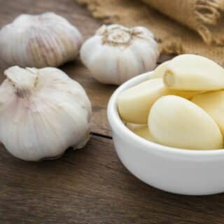 A bowl of peeled garlic next to three whole heads of unpeeled garlic.