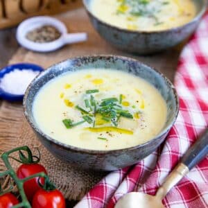 Delicious leek and potato soup, garnished with oil, chives and black pepper, with tomatoes on the vine alongside.