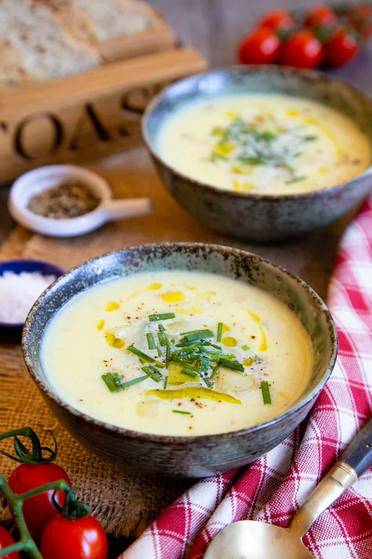 Creamy leek and potato soup, dotted with oil and garnished with snipped chives, elegant and simple served in stylish stoneware bowls