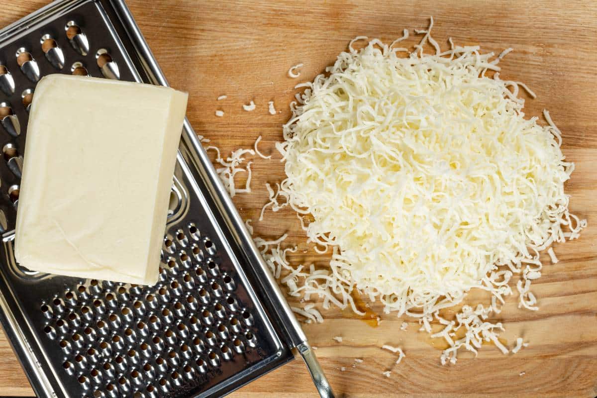 A block of low moisture mozzarella on a grater, next to a pile of grated cheese.