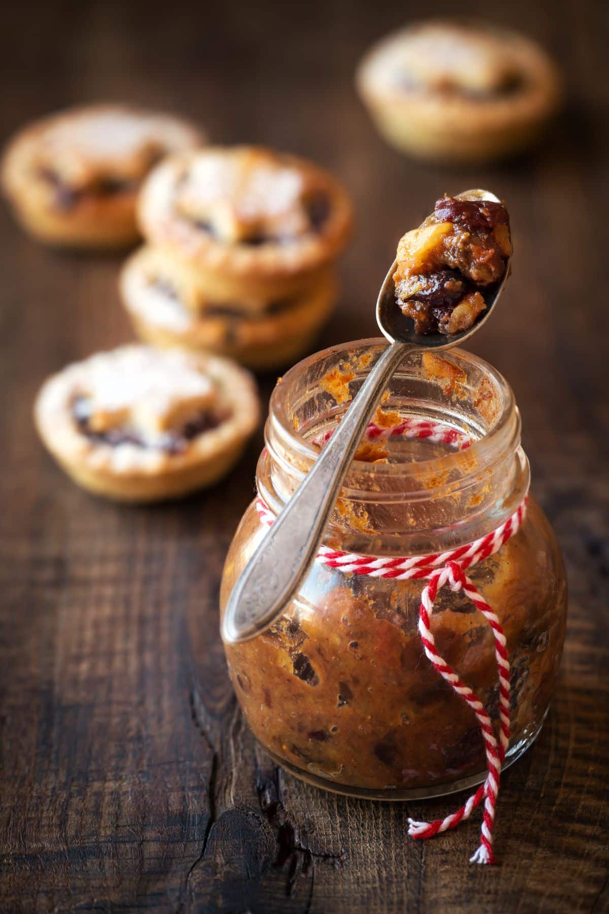 An open jar of mincemeat and a spoon, with mince pies behind