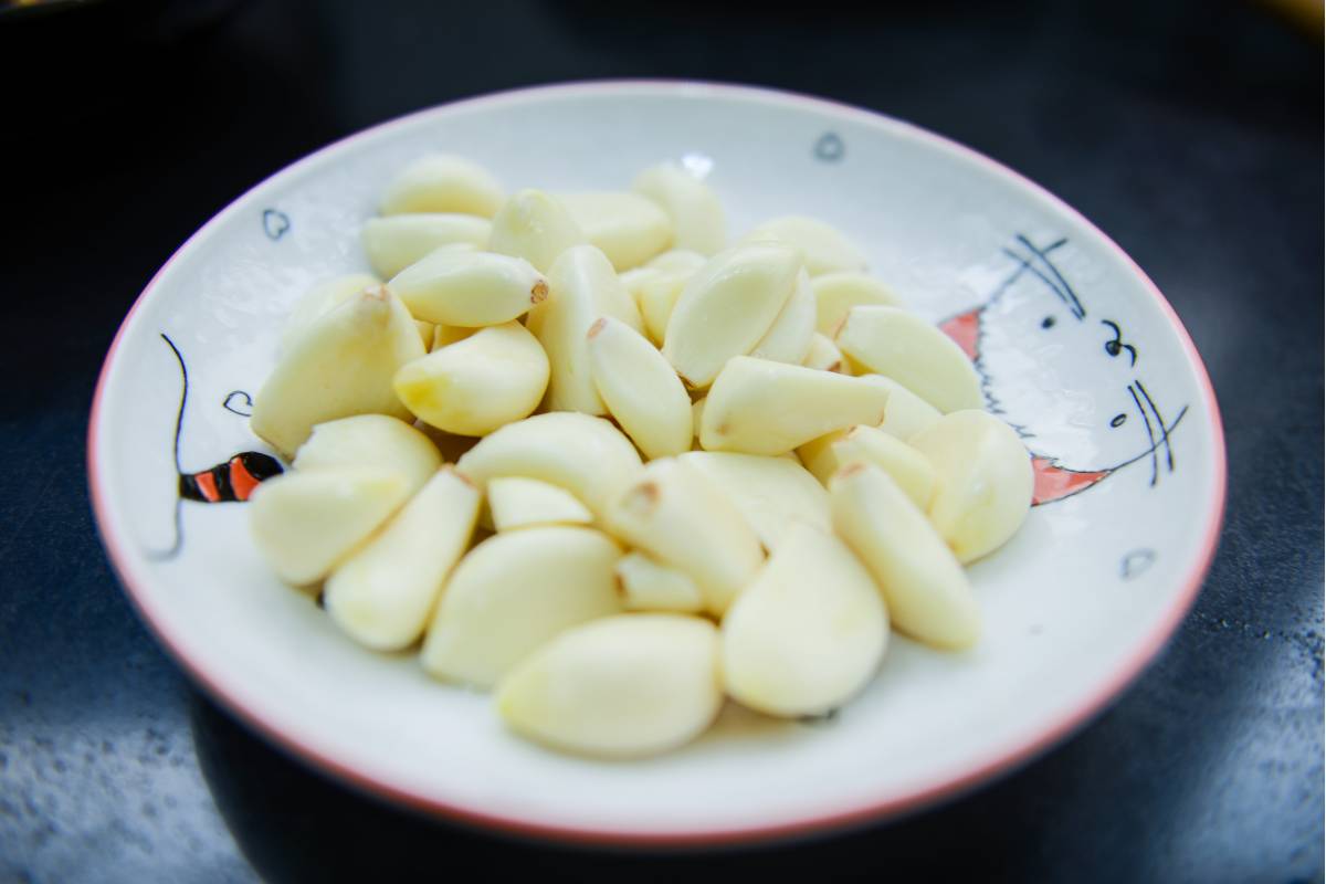 A plate of peeled garlic cloves. The plate is sitting on a black background.
