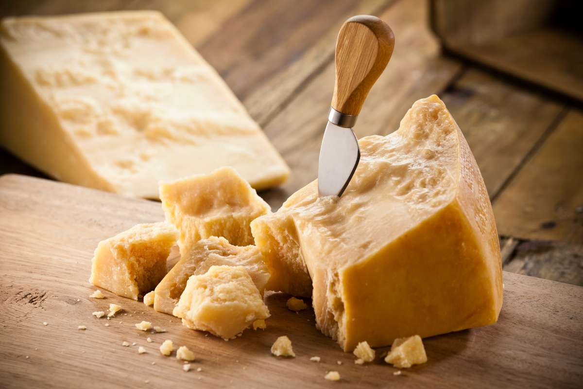 A block of hard Parmesan cheese, with a knife sticking out. The cheese is on a wooden board.