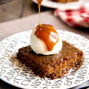 Sticky toffee pudding served in a neat square with ice cream and extra sauce.