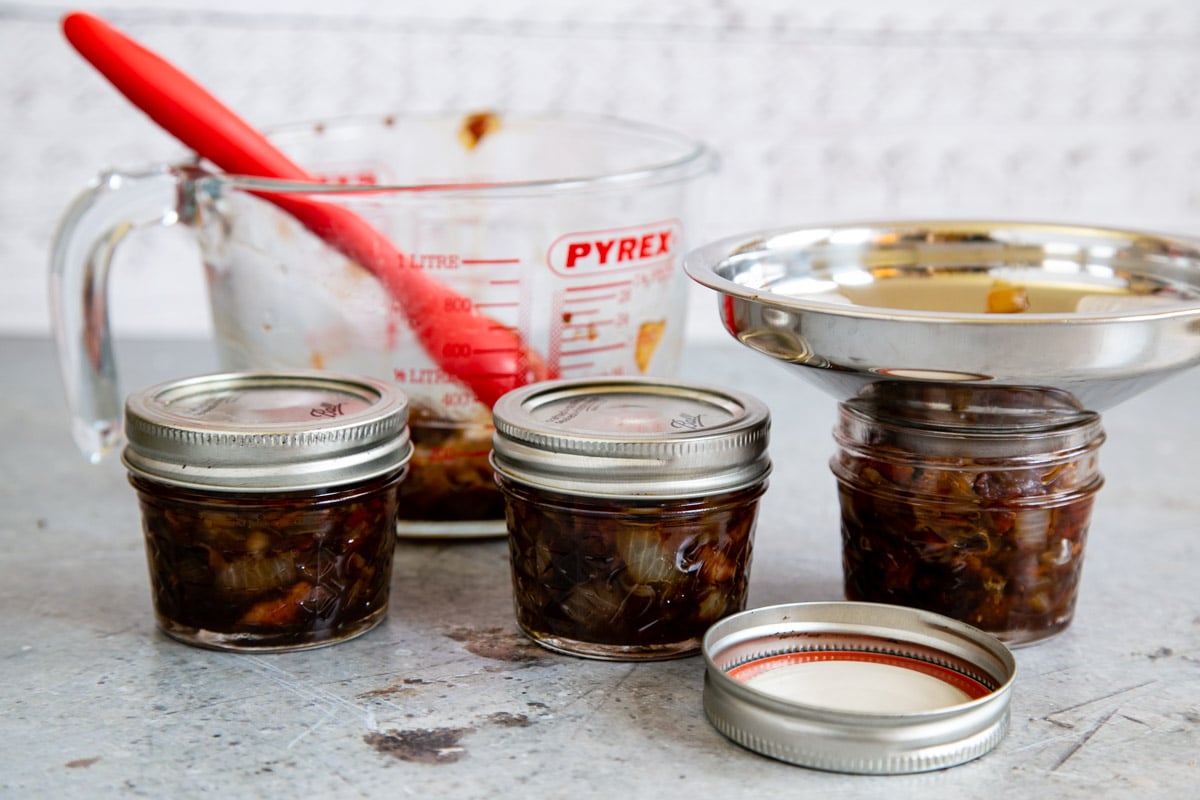 Using a jam funnel to fill the jars with tomato and bacon jam